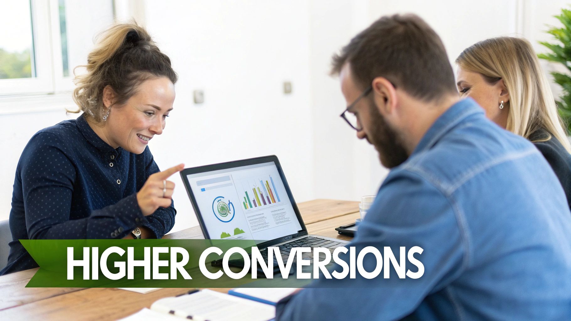 A smiling woman points at a laptop displaying data charts to two colleagues during a business meeting.
